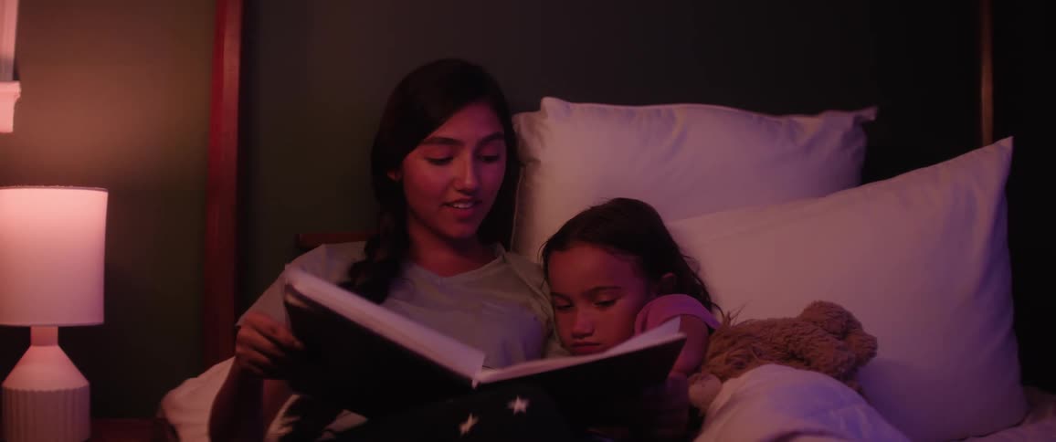 A mother reads a bedtime story to her daughter in a cozy dimly lit bedroom