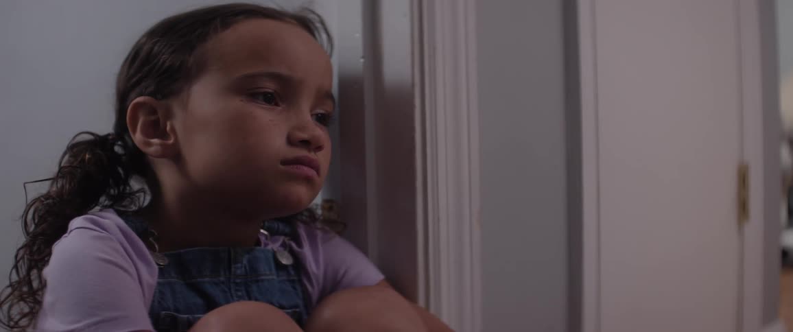 The face of a sad little girl who is sitting next to a white door and is thoughtful