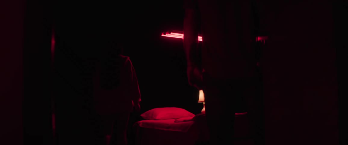 A girl enters the dark room with red light and a man slowly closes the door
