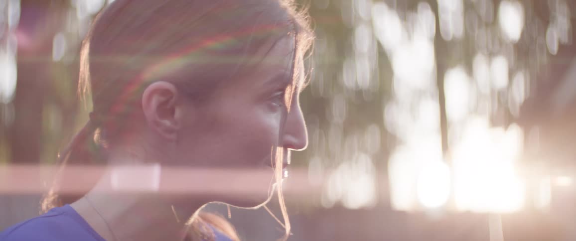 Two women sit facing each other and talk with trees and sunlight softly blurred in the background