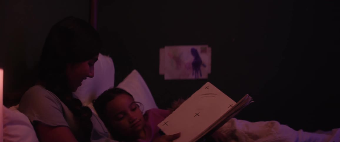 Mother lying in bed with her little daughter reading a book