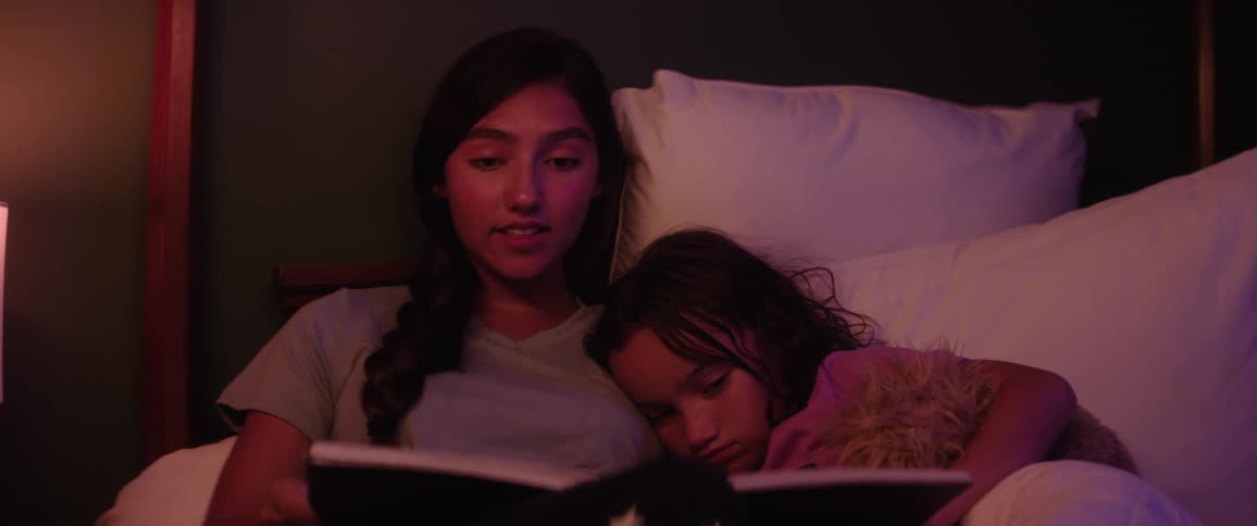 Mother reads a story to her daughter while they both relax in bed