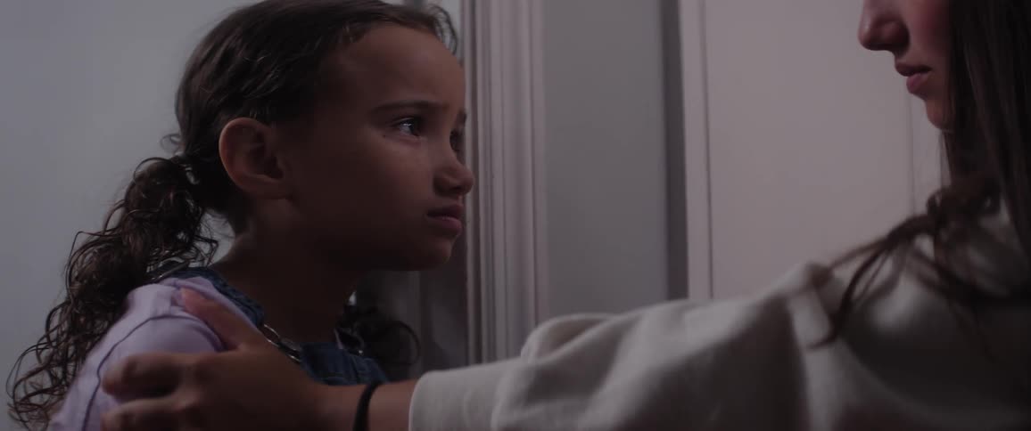 Woman gently holds a childs shoulders in a dimly lit hallway offering a calm and reassuring presence