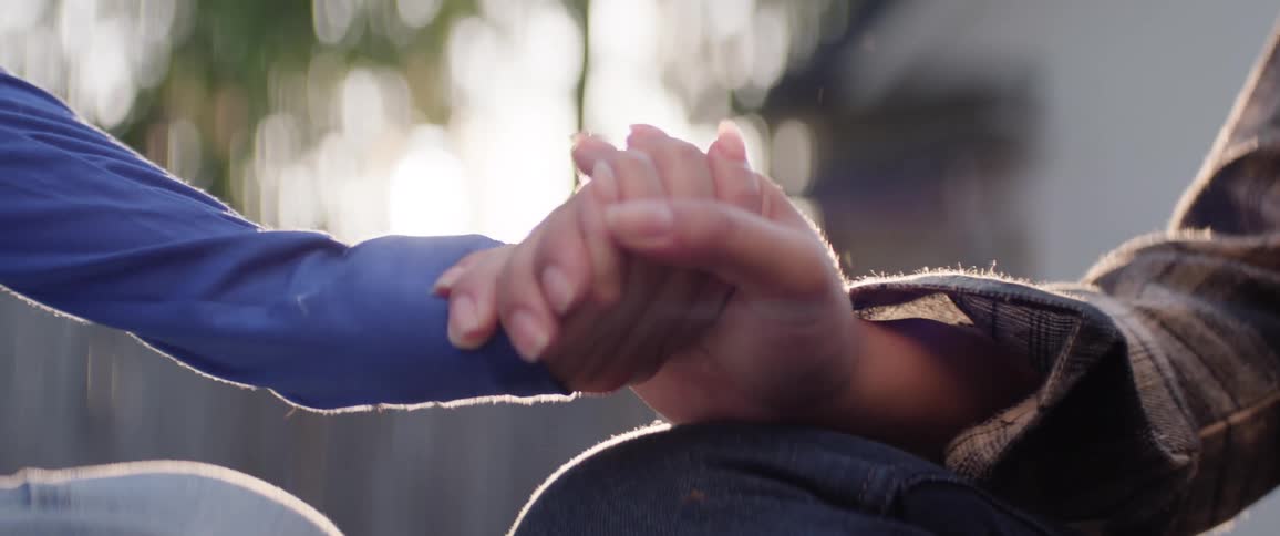 Close up of two girls holding hands while sitting outdoors during daytime