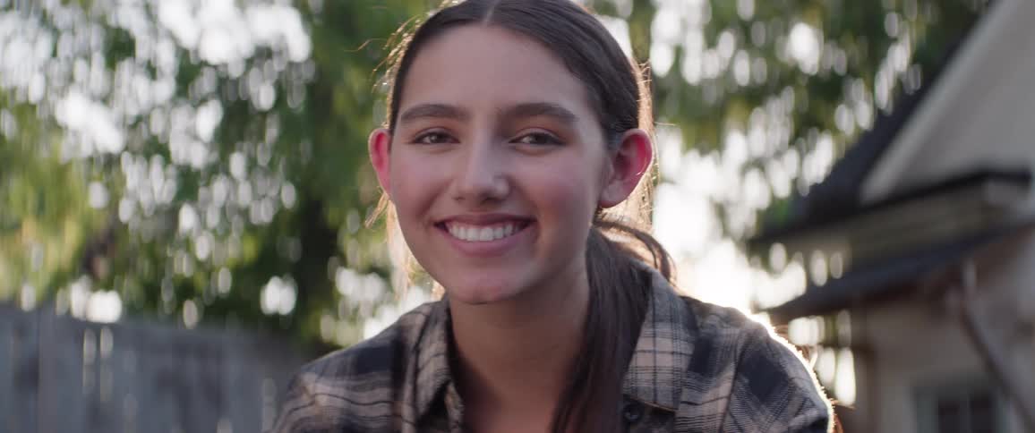 A woman in profile looks towards the camera smiling with sunlight shining behind her