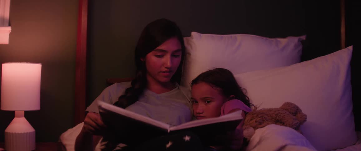 Female teen reads a book to her younger sister in bed at night before bedtime