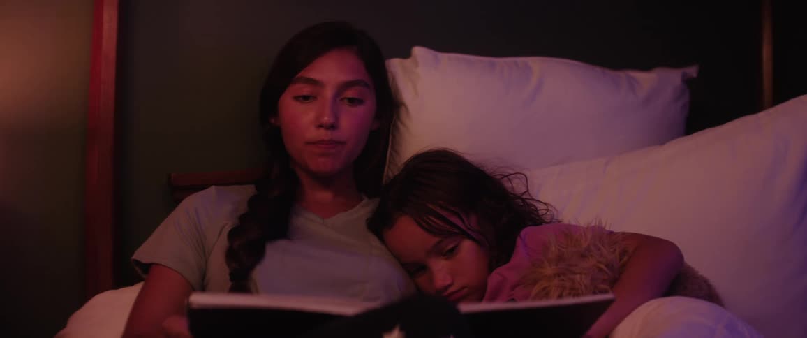 Daughter follows along in a book her mother is reading to her in bed