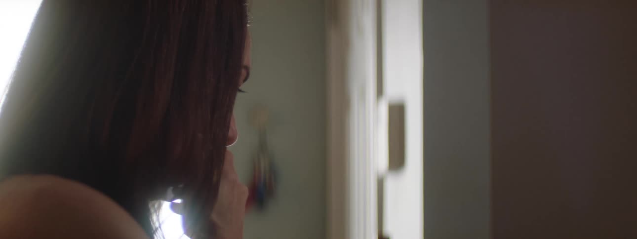 Sad woman with brown hair sits in a room eyes closed and hand near her mouth as she cries