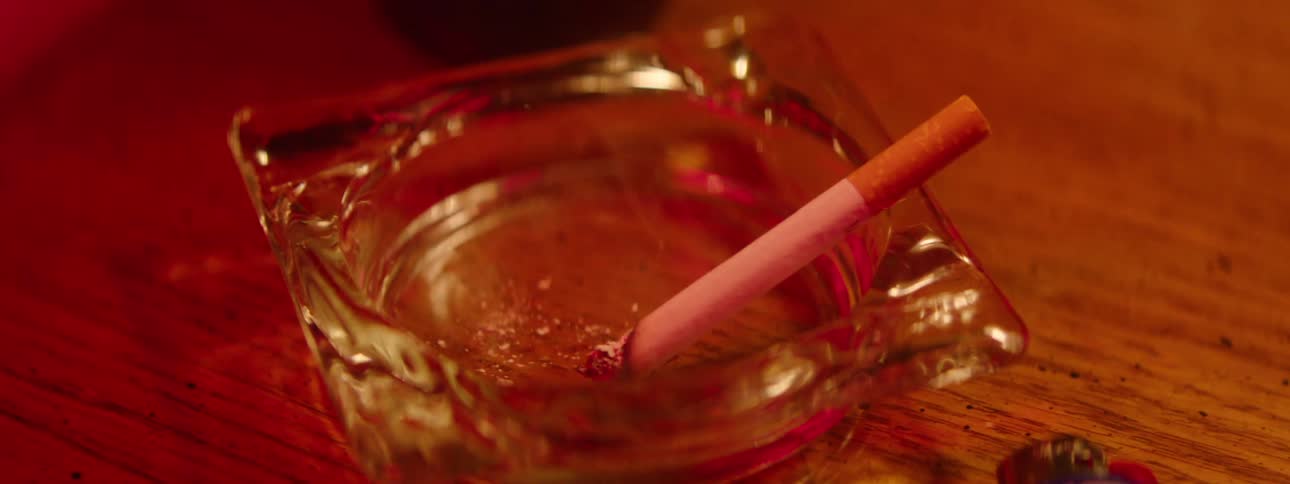 A lit cigarette is in a glass ashtray and smoke is coming out of it