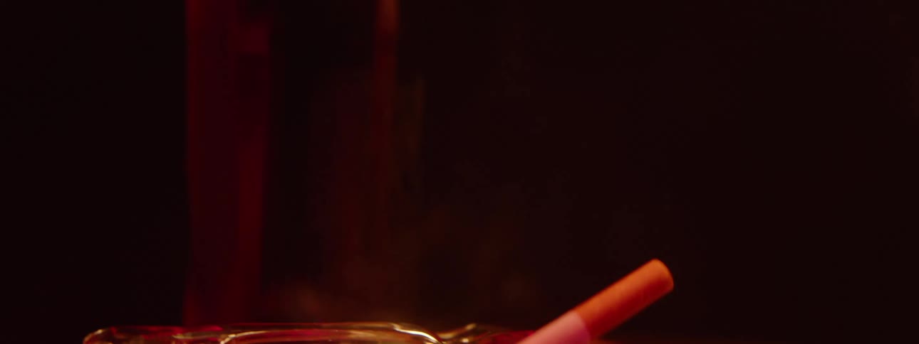 Close up of a burning cigarette placed in a glass ash tray on a table