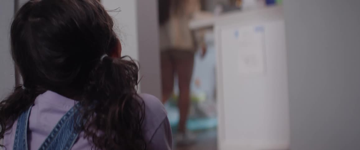 A young woman stands up from the floor where she was sitting facing a child and walks away inside the house leaving the child behind