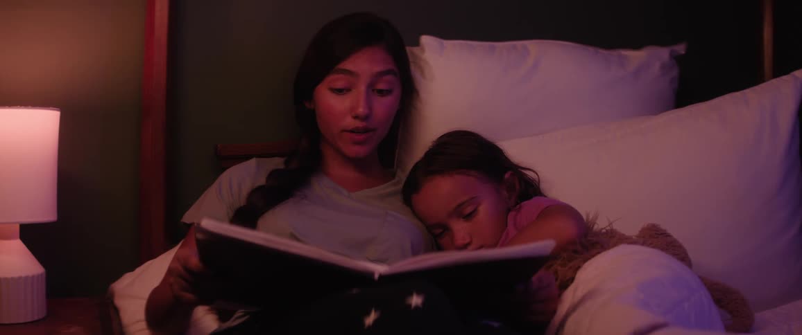Teenage girl reads a book to her younger sister in bed at night before bedtime