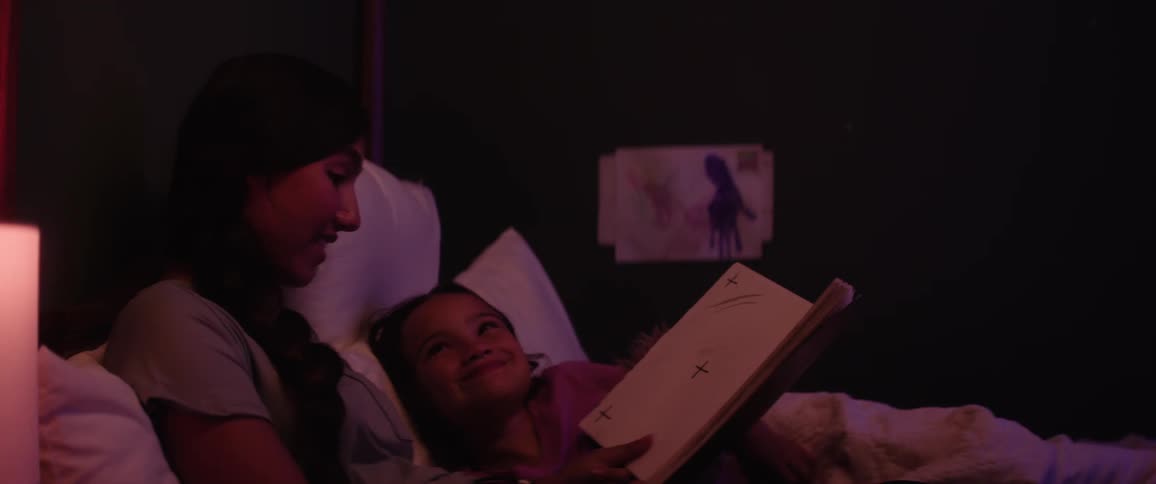 Close up of a female teenager reading a book to a girl in bed at night before bedtime