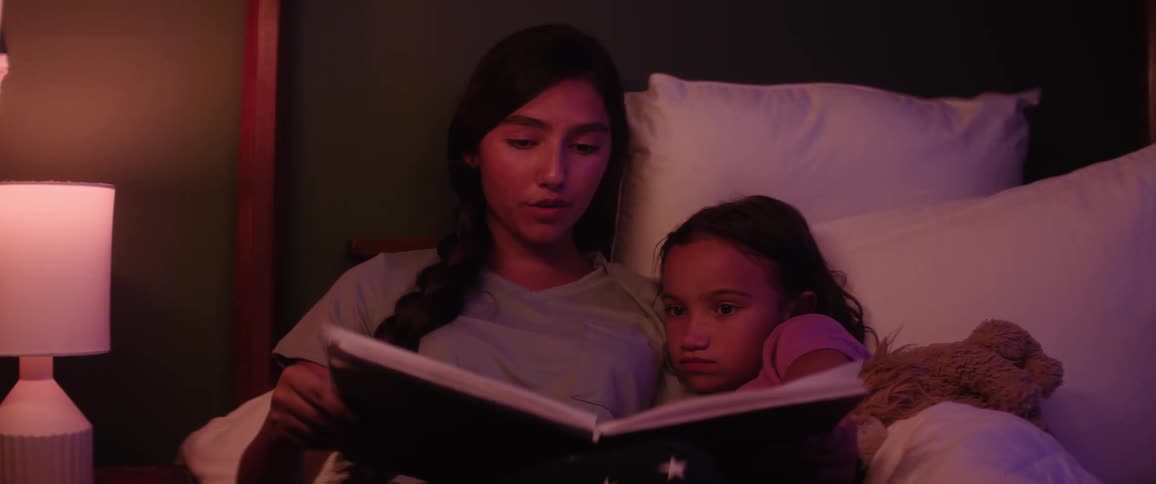 Female teenager reads to her younger sister in bed at night