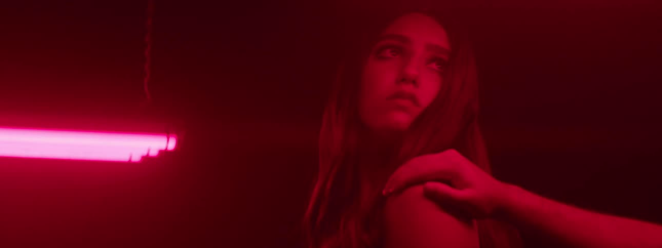 A young woman looks at a red fluorescent bulb illuminating the dark room she is touched on the shoulder and turns with a sad expression to see who is touching her