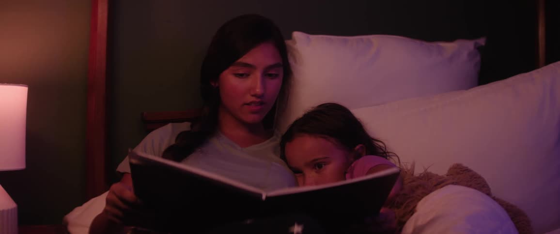 Female teen reads a book to her younger sister in bed at night before bedtime
