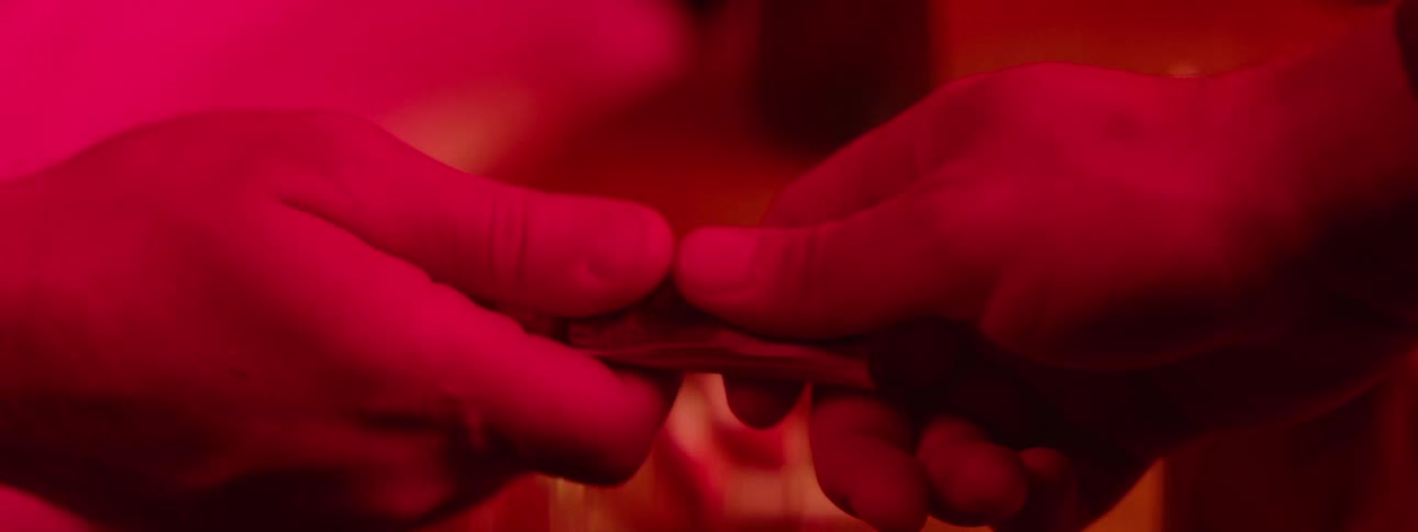 Close up of two hands as two people exchange paper currency in a red lit room