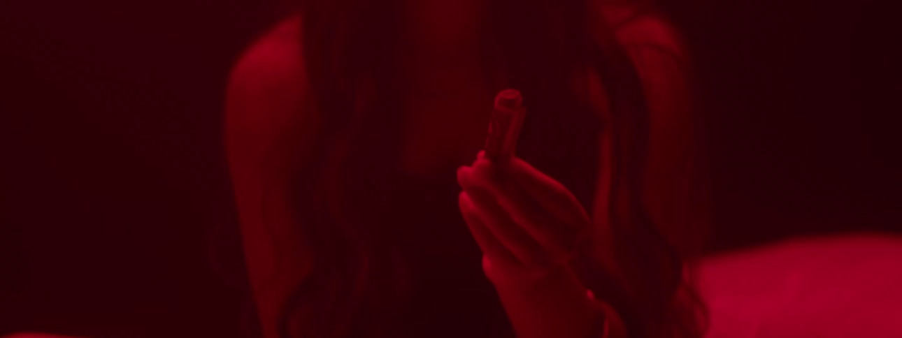 A young woman in a room bathed in red light lowers her hand while holding an object