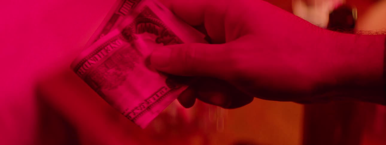 Close up of two hands as two people exchange money in a red lit room