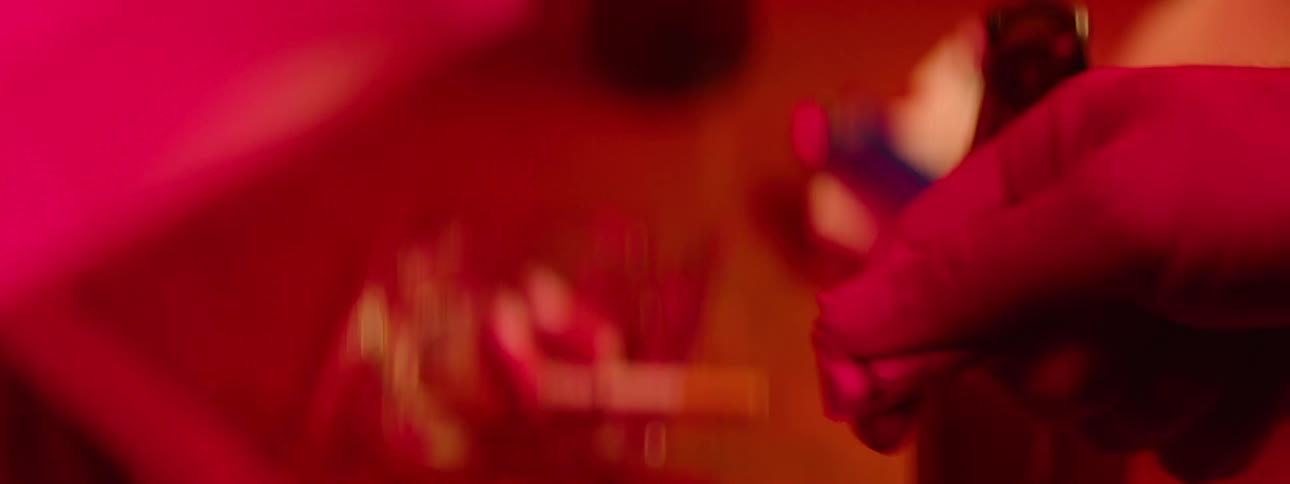 Two hands under red lighting exchange a rolled up dollar bill