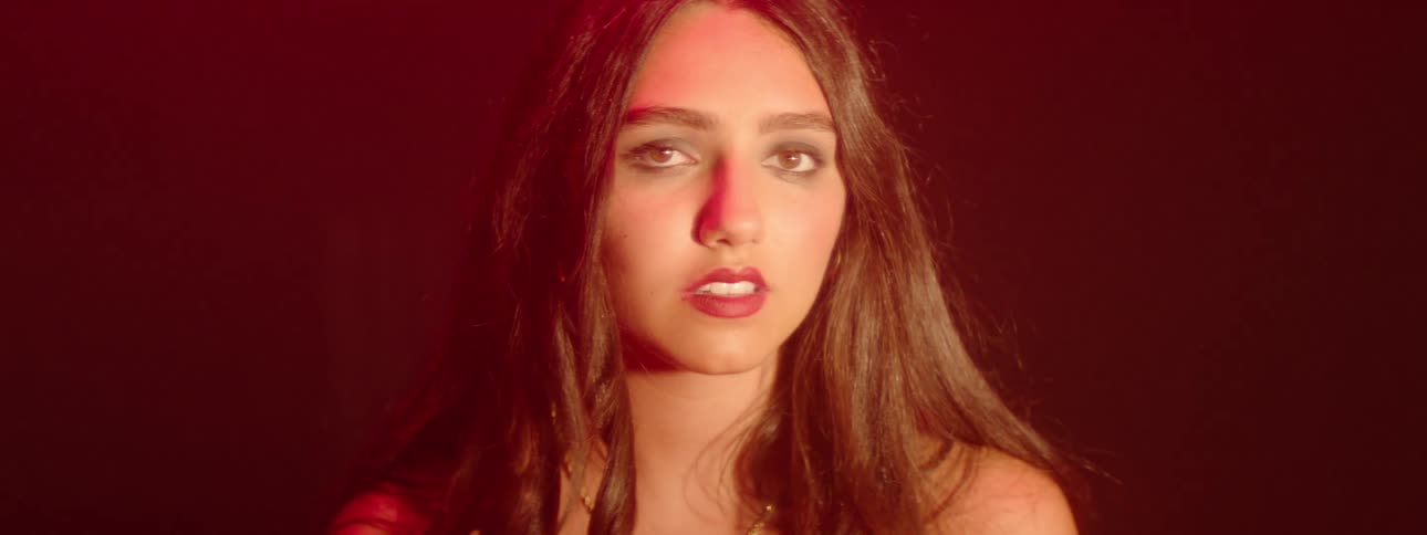 The face of a young woman who is staring straight ahead and in an indoor environment with a red light illuminating her face