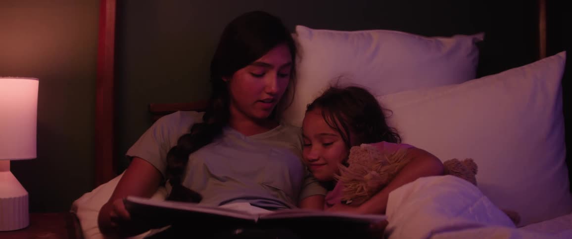 Two sisters cuddle in bed while reading a bedtime story sharing a quiet and loving moment