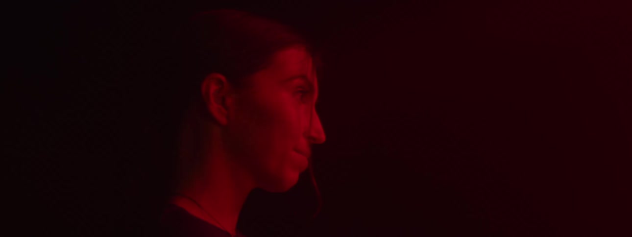 A person stands in profile lit by intense red lighting against a dark background
