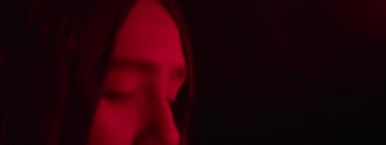 A young woman is illuminated by intense red lighting her expression calm and contemplative as she gazes ahead in the darkness