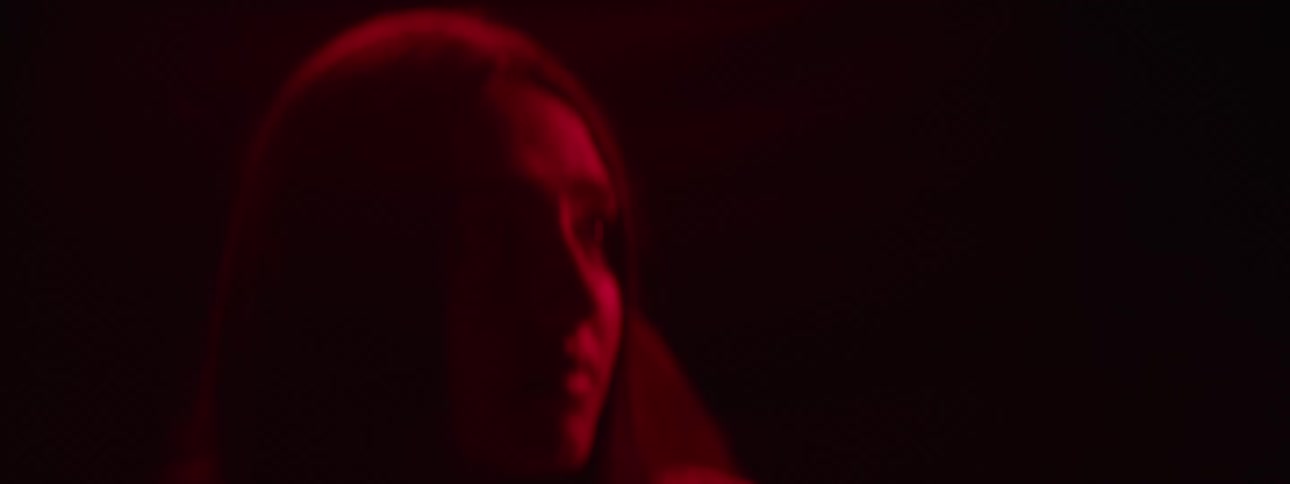 Woman under a red fluorescent light stares ahead nervously