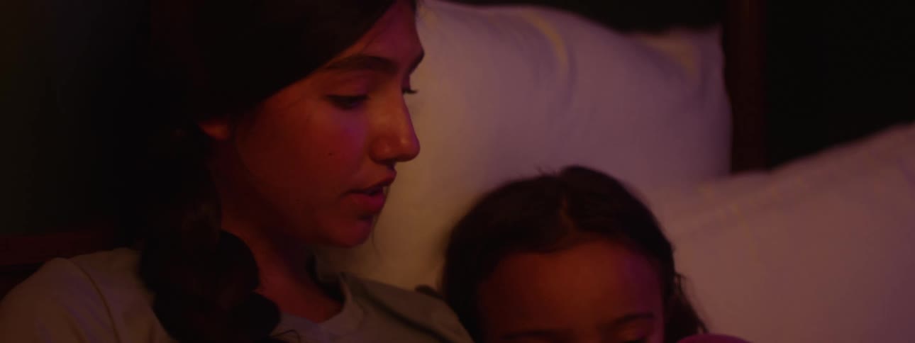 The teenager is reading to her sister in bed