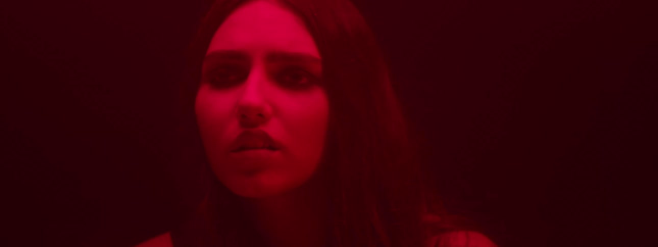 A young woman suddenly wakes up from sleep looking fearful in a room illuminated by deep red light