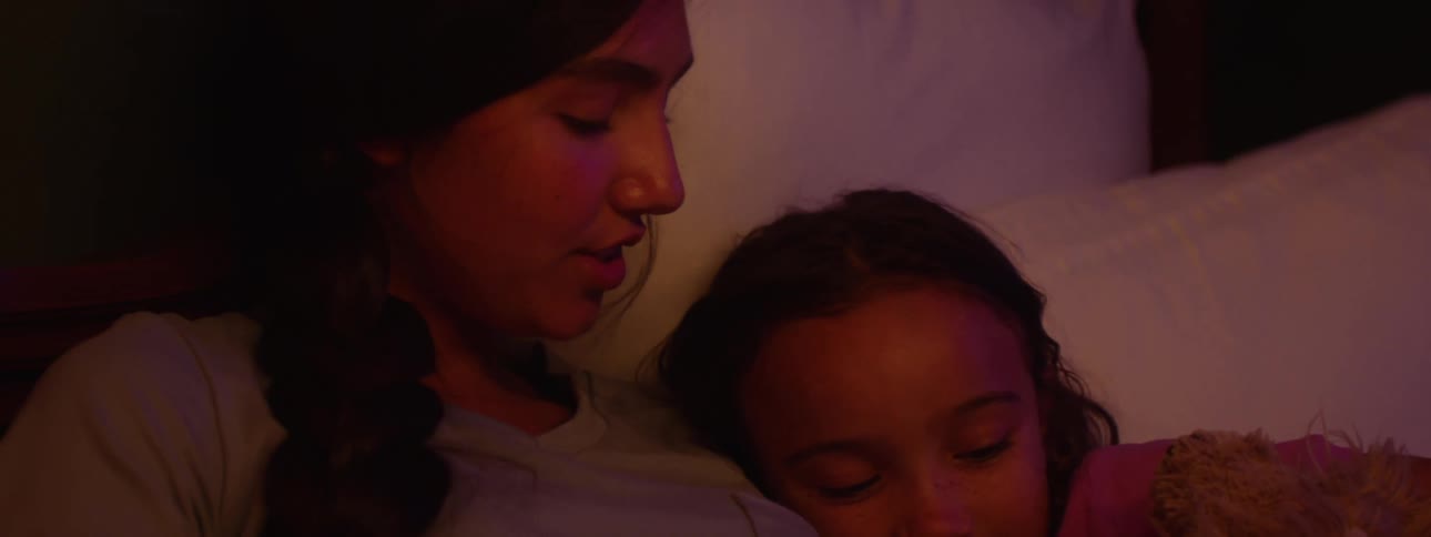 Female teen reads to her younger sister in bed at night before bedtime