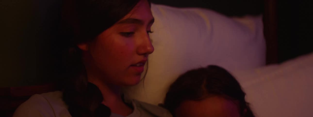 A woman holds a child with long dark hair who is resting her head on the womans chest and looking at an open book