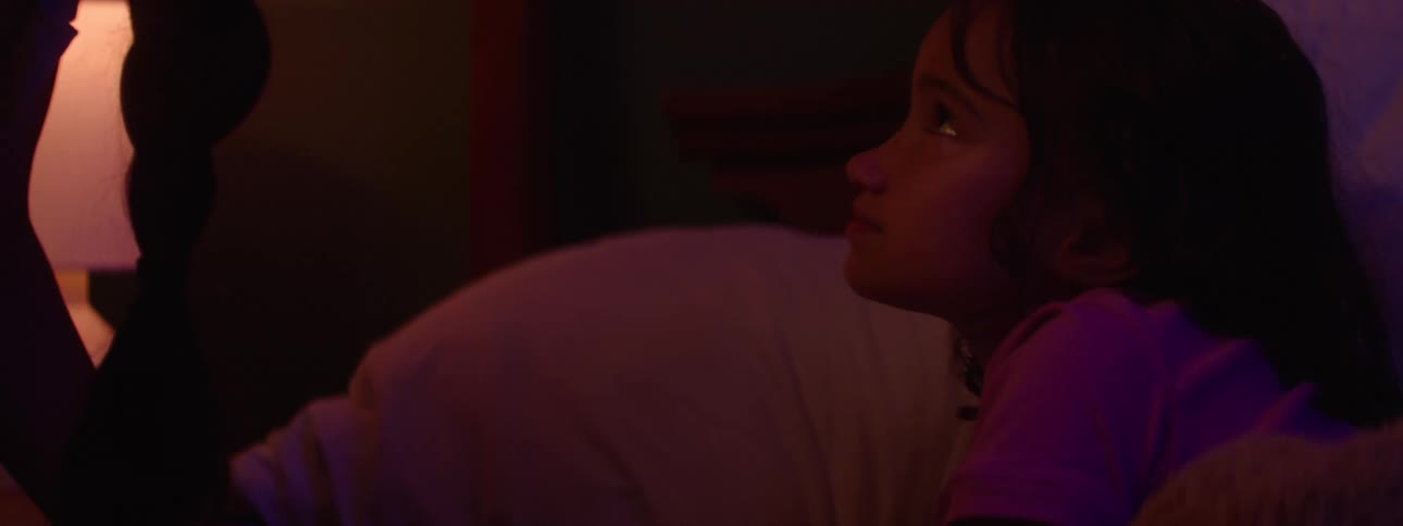 In a dimly lit room a young woman and a child lie in bed and make a pinky promise