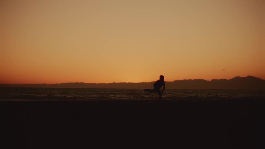 A person throws a ball playfully on the beach at sunset