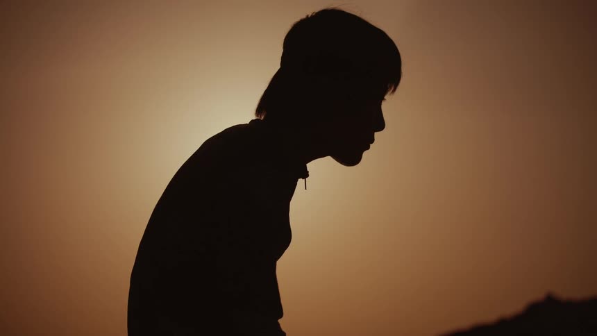 A man in profile is silhouetted against an orange and brown sky