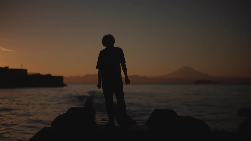 A boy stands on the bank of a river staring at the flowing water as dusk turns to night