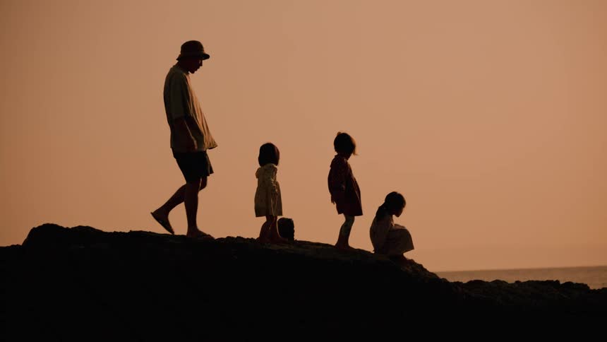 Silhouetted adult and three kids stand on a hill at sunset