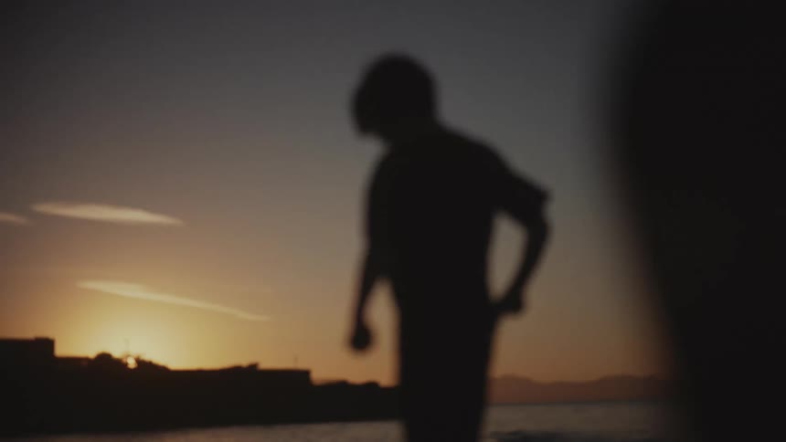 A child dances outdoors at sundown moving their arms left and right