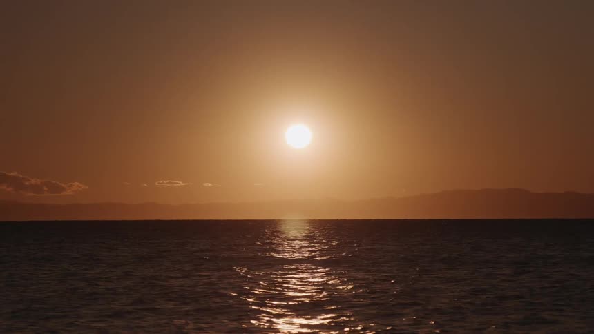 Sun hovering in the sky over mountains and ocean