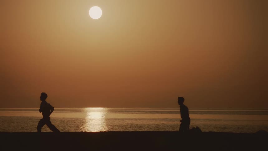 Two people jogging along the coast of the beach as the sun sets