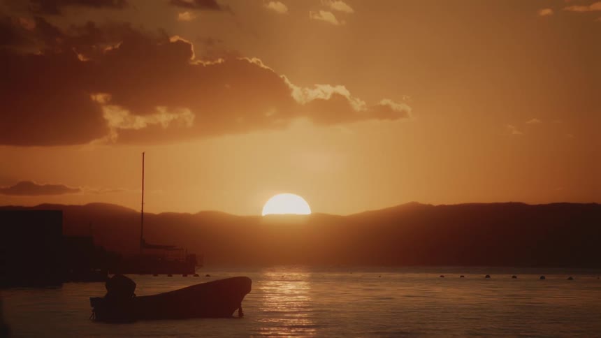 The sun is rising on the shore where a boat is anchored
