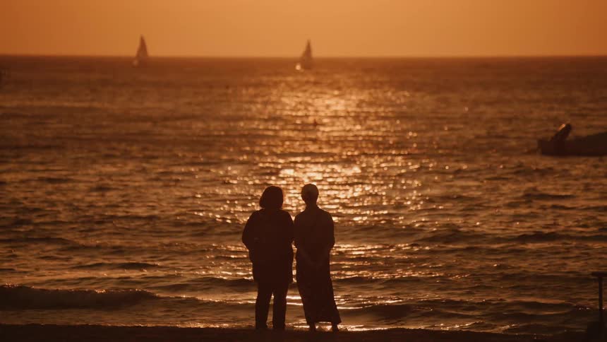 Two people stand on the beach watching the sunset over the ocean