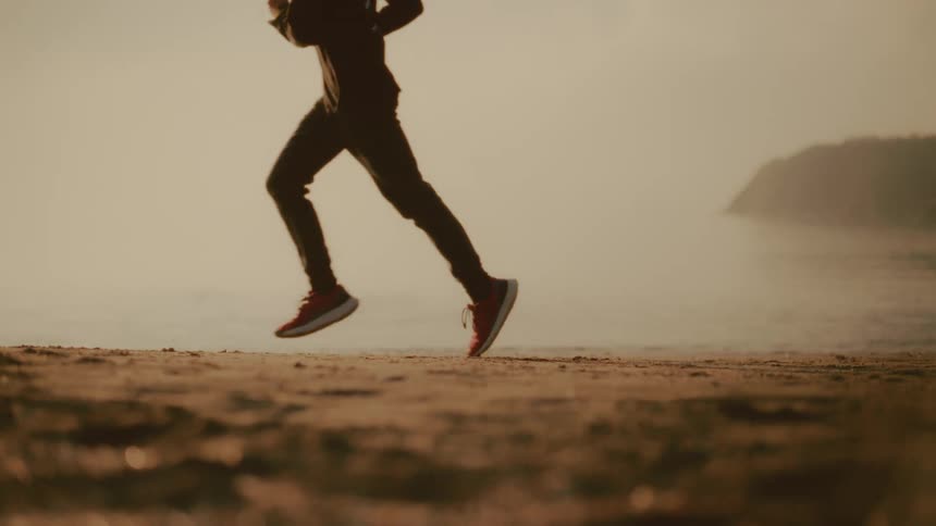 People jog across a foggy beach with a rocky cliff faintly visible in the background