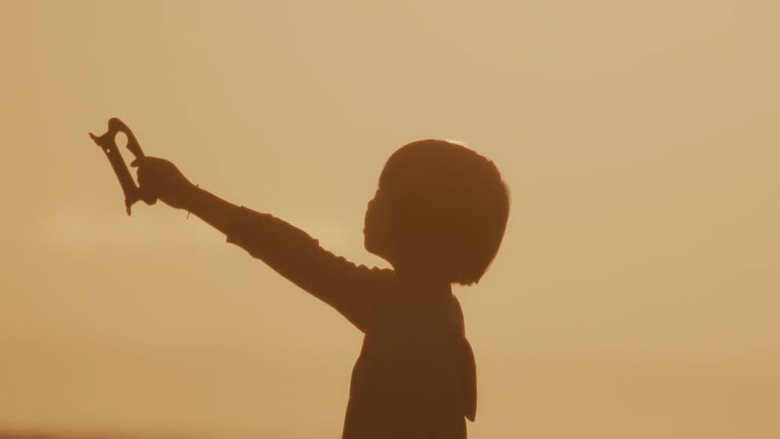 A girl is flying a kite on the beach at sunrise