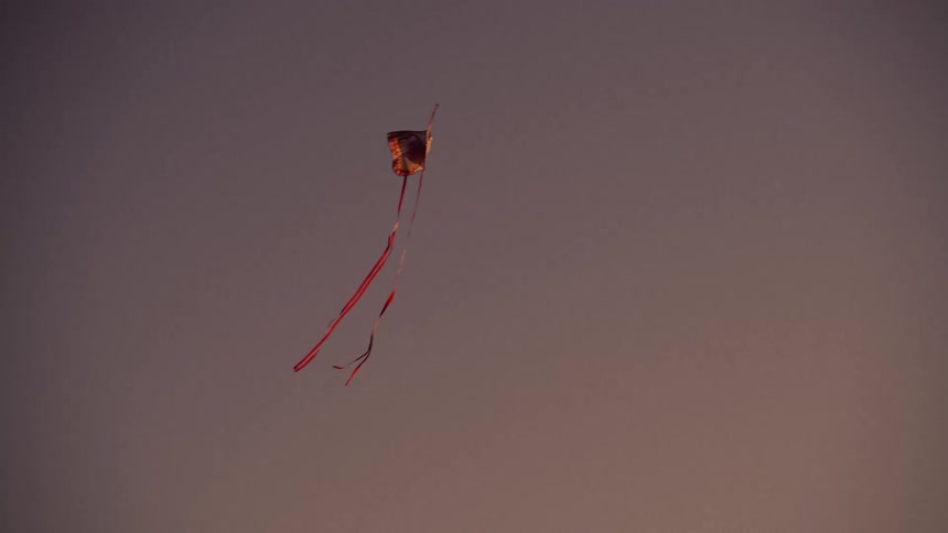 An orange butterfly kite with two red ribbon streamers is lazily floating in the wind to and fro