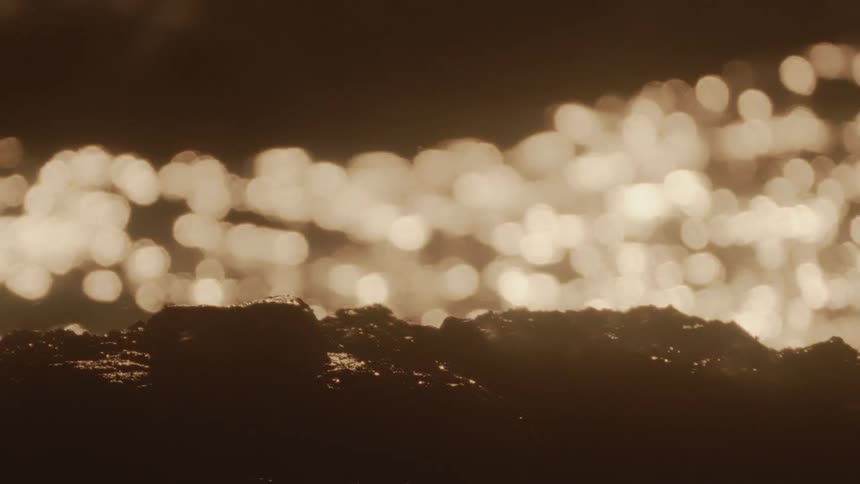 Reflection of the sun in an ocean with rocks in the foreground