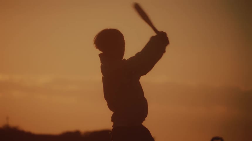 Teenage boy holding a baseball bat and taking a swing under a sunset sky