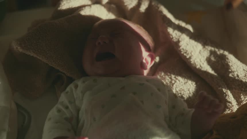 A baby lies on a blanket crying while lit by warm natural light