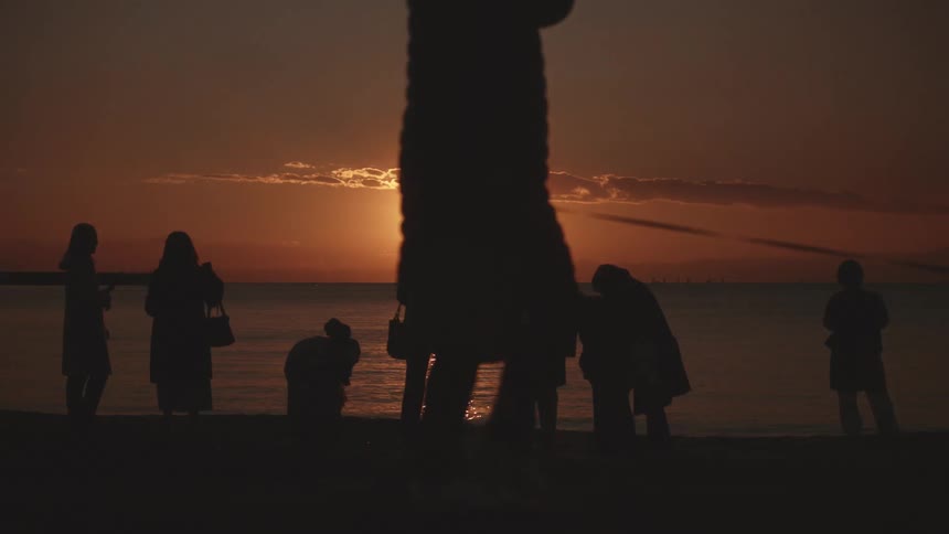 Back of people standing close to the sea water at sunset